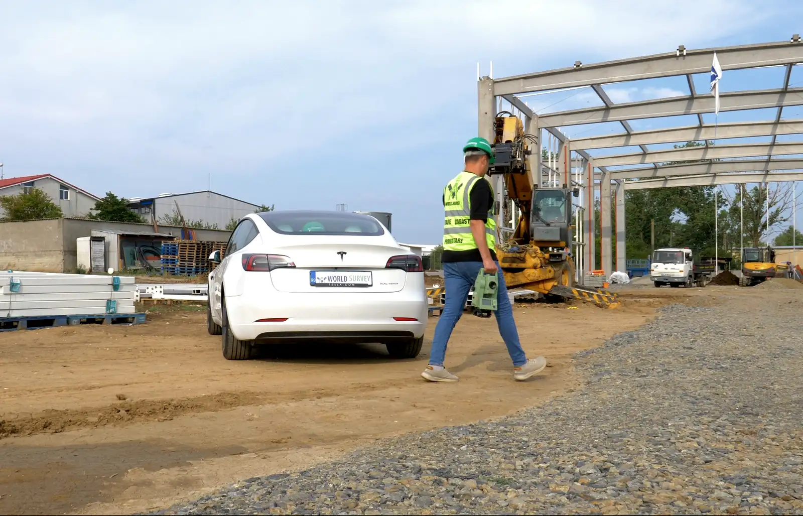 Topograf World Survey cu stația totală în mână, pe șantierul unei hale cu structură de beton.
