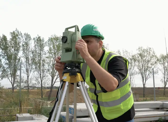 Topograf World Survey cu cască verde, vizând prin stația totală pe trepied.